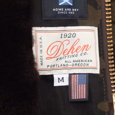 תקריב על תווית בגד לבנה עליה מודפס הכיתוב Made in USA בלבן וכחול, כשהיא תפורה לבד דנים כהה, המייצגת את הסטנדרט החדש של שקיפות וייצור מקומי בתעשייה.